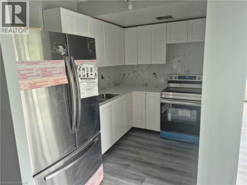 Kitchen featuring white shaker cabinetry, stainless steel appliances, a white marble-look backsplash, white countertops, and wood-finish flooring - 150 Charlton Avenue E Unit# 708, Hamilton, ON 