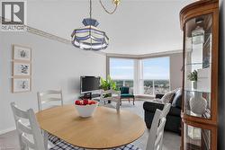 Open-concept living area featuring a prominent bay window, light wood-finish flooring, a decorative ceiling light fixture, and a built-in display cabinet with glass shelving - 