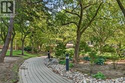 Paved pathway bordered by decorative river rock, mature trees, and landscaping - 