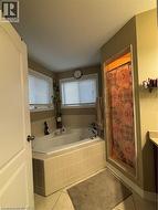 Corner soaking tub with tiled surround, two windows with blinds, tiled flooring, and a separate shower alcove - 