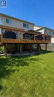 Expansive backyard featuring a large raised wooden deck with black balusters and a gravel patio beneath - 