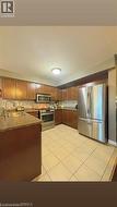 Kitchen featuring brown wood cabinetry, stainless steel appliances, speckled countertops, and a tiled backsplash - 