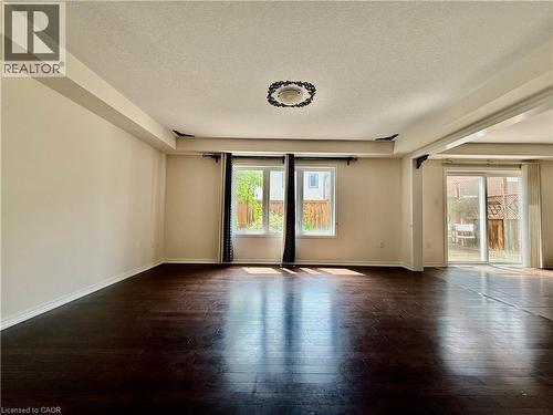 Spacious room featuring dark wood-finish flooring, two large windows, and sliding glass doors providing outdoor access - 386 Apple Hill Crescent, Kitchener, ON 