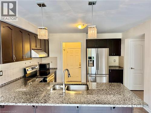 Kitchen featuring a large island with an undermount sink, dark wood-finish cabinetry, stainless steel appliances, and tile backsplash - 386 Apple Hill Crescent, Kitchener, ON 