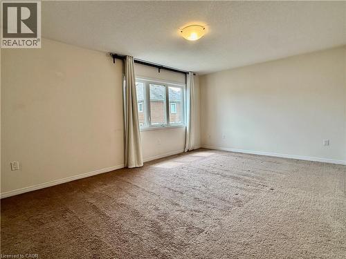 Spacious room featuring broadloom carpet flooring, multiple windows, light beige wall paint, white trim, and an overhead flush-mount light fixture - 386 Apple Hill Crescent, Kitchener, ON 