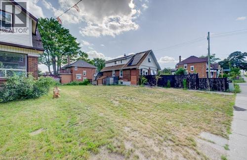 Expansive cleared lot with mature trees in the background, featuring a partial sidewalk and existing perimeter fencing - 153 Courtland Avenue E, Kitchener, ON 