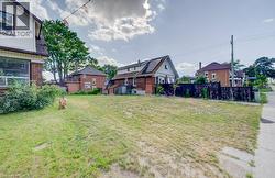 Expansive cleared lot with mature trees in the background, featuring a partial sidewalk and existing perimeter fencing - 