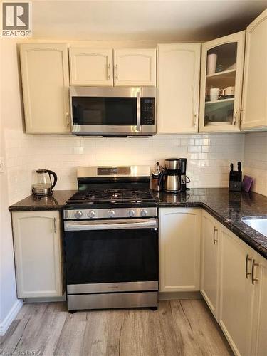 Modern kitchen featuring a stainless steel range with overhead microwave, ample upper and lower cabinetry, dark stone countertops, and wood-finish flooring - 86 North Park Street, Brantford, ON 