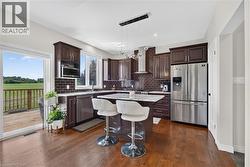 Gourmet kitchen featuring wood-finish flooring, dark wood cabinetry, stainless steel appliances, and a central island with a stone countertop - 