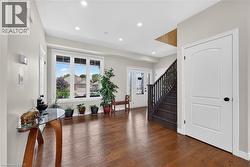 Bright entry foyer featuring wood-finish flooring, recessed lighting, a multi-pane window, dark-stained staircase with wood balusters, and a white interior door - 