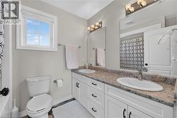 Bathroom featuring a double vanity with stone-finish countertops, undermount sinks, and white cabinetry with black hardware - 