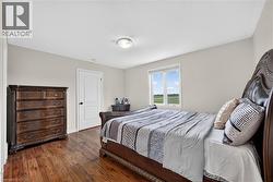 Bedroom featuring wood-finish flooring, a white interior door, a window with exterior scenery, and neutral wall paint - 