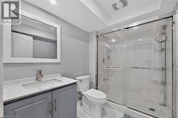 Contemporary bathroom featuring a spacious glass-enclosed shower with white tile surround, a vanity with a white countertop and gray cabinetry, a rectangular mirror, and recessed lighting - 