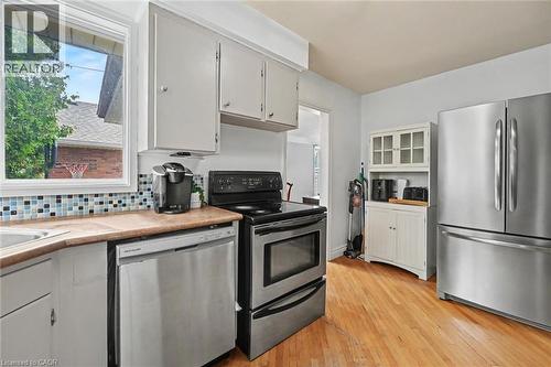 Kitchen featuring stainless steel appliances, light wood-finish flooring, white cabinetry, a mosaic tile backsplash, and a window above the sink - 56 Everton Place, Hamilton, ON 