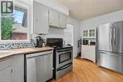 Kitchen featuring stainless steel appliances, light wood-finish flooring, white cabinetry, a mosaic tile backsplash, and a window above the sink - 