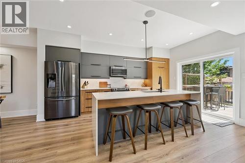 Contemporary kitchen featuring wood-finish flooring, a stainless steel refrigerator, and sleek flat-panel cabinetry - 63 Plymouth Road, Kitchener, ON 