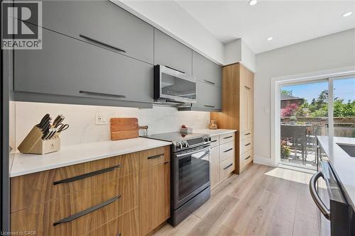 Modern kitchen featuring two-tone cabinetry, stainless steel appliances, white countertops, and wood-finish flooring - 63 Plymouth Road, Kitchener, ON 