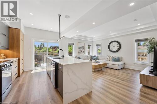Open-concept living space with wood-finish flooring, a kitchen island featuring a waterfall-edge countertop, and a built-in oven range - 63 Plymouth Road, Kitchener, ON 