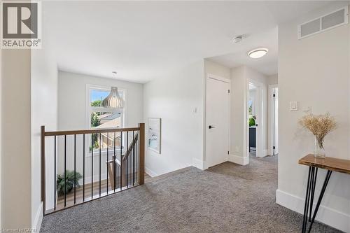 Carpeted hallway with a wood-finish and black metal spindle railing overlooking a staircase - 63 Plymouth Road, Kitchener, ON 