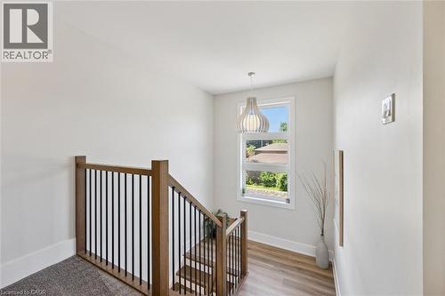 Stairwell featuring wood-finish railings with black balusters, a large white-framed window, and a hanging pendant light fixture - 63 Plymouth Road, Kitchener, ON 