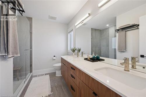 Double vanity with integrated sinks and white countertops, wood-finish cabinetry, a large frameless mirror, and a glass-enclosed shower with tiled walls - 63 Plymouth Road, Kitchener, ON 