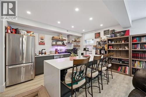 Modern kitchen area featuring a large center island with seating, recessed lighting, wood-finish flooring, stainless steel appliances, and open shelving - 63 Plymouth Road, Kitchener, ON 