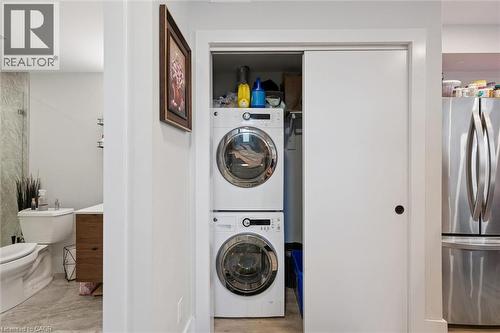 In-unit stackable washer and dryer, white sliding closet door with matte black hardware, and stainless steel refrigerator - 63 Plymouth Road, Kitchener, ON 