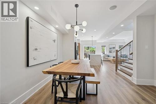 Open-concept living space featuring wood-finish flooring, recessed lighting, a contemporary chandelier, a staircase with dark wood treads and white risers, and a kitchen island with a waterfall counte - 63 Plymouth Road, Kitchener, ON 