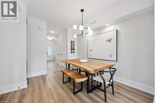 Dining area featuring wood-finish flooring, a contemporary chandelier, recessed lighting, and crisp white walls with matching baseboards - 63 Plymouth Road, Kitchener, ON 