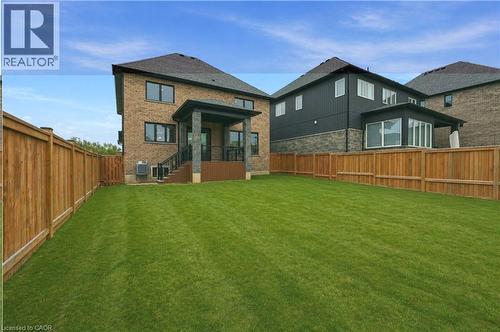 Expansive lawn featuring a covered porch with stone columns and black railings, light brown privacy fencing, and a brick and siding exterior - 7 Bartlett Avenue, Grimsby, ON 