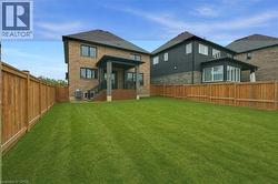 Expansive lawn featuring a covered porch with stone columns and black railings, light brown privacy fencing, and a brick and siding exterior - 