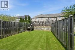 Expansive green lawn area featuring wood privacy fencing, a tiered design with a retaining wall, and a wooden staircase - 