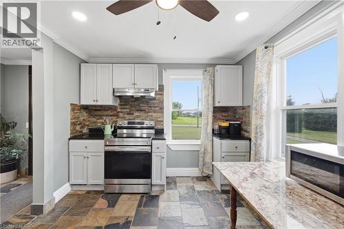 Kitchen featuring light gray cabinetry, dark countertops, a stacked stone backsplash, stainless steel appliances, and multi-toned slate flooring - 97 Smith Road, Hamilton, ON 