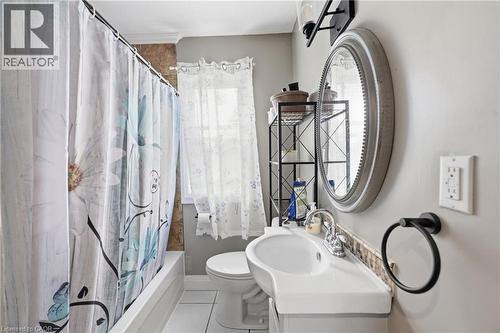 Bathroom featuring a single vanity with an integrated sink, a circular framed mirror, and a tub with a shower - 97 Smith Road, Hamilton, ON 