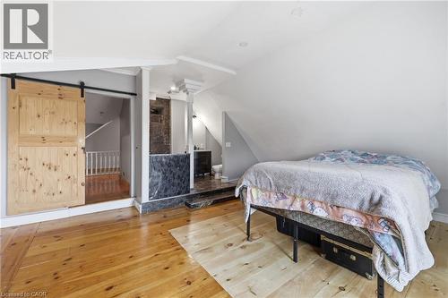Natural wood-finish flooring extending into an open-concept space featuring a sliding barn door, a partial stone wall, and a raised platform with a dark vanity - 97 Smith Road, Hamilton, ON 