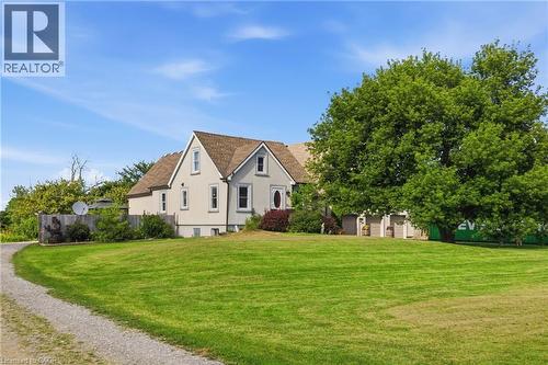 Gable-roof property featuring a light-colored exterior with white trim, a gravel driveway, and a spacious green lawn - 97 Smith Road, Hamilton, ON 