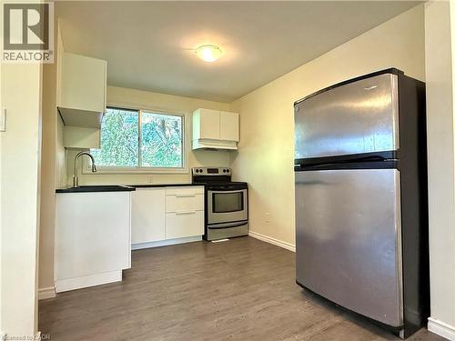 Kitchen featuring wood-finish flooring, stainless steel appliances, white cabinetry, dark countertops, and a window with exterior tree views - 62 Bond Street Unit# 3, Kitchener, ON - Indoor Photo Showing Kitchen