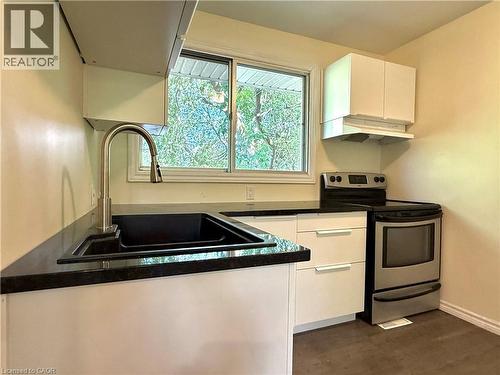 Modern kitchen featuring sleek white cabinetry, dark countertops, a stainless steel electric range, and a contemporary sink with a gooseneck faucet - 62 Bond Street Unit# 3, Kitchener, ON - Indoor Photo Showing Kitchen With Double Sink