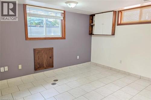 Spacious room featuring white tile flooring, two windows with wood-finish frames, a flush-mount ceiling light fixture, and a wall-mounted storage cabinet - 98 Kipling Road Unit# 2, Hamilton, ON 