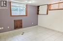 Spacious room featuring white tile flooring, two windows with wood-finish frames, a flush-mount ceiling light fixture, and a wall-mounted storage cabinet - 98 Kipling Road Unit# 2, Hamilton, ON 