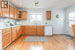 Kitchen featuring wood-finish cabinetry, white countertops, stainless steel sink, wood-finish flooring, and a dishwasher - 