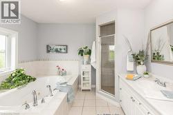 Bathroom featuring a built-in soaking tub with deck-mounted fixtures, a glass-enclosed shower, a white vanity with an integrated sink, and square tile flooring - 