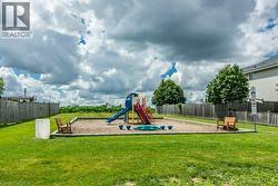 Expansive green lawn surrounds a dedicated play area featuring a composite playset with slides and steps, contained within a wood-bordered gravel bed - 