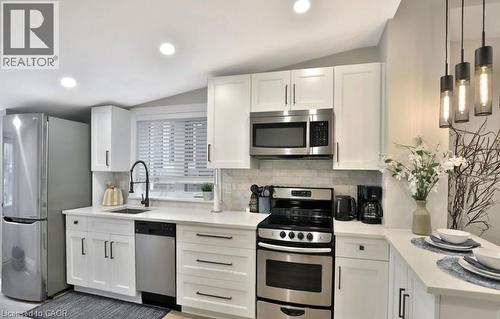 Bright kitchen featuring white shaker cabinetry, stainless steel appliances, a tile backsplash, and recessed lighting - 33 Hawthorne Avenue, Hamilton, ON 