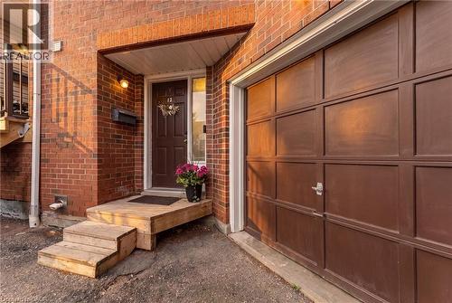 Brick exterior with an attached garage featuring a panel door, wooden steps leading to the main entrance, and an outdoor wall light fixture - 465 Beechwood Place Unit# 12, Waterloo, ON - Outdoor With Exterior