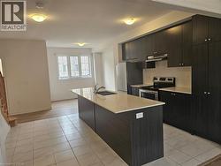 Kitchen featuring appliances with stainless steel finishes, light tile patterned floors, a kitchen island with sink, modern cabinets, and under cabinet range hood - 