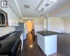 Open-concept kitchen featuring white cabinetry, dark countertops, stainless steel appliances, and wood-finish flooring - 