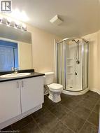 Bathroom featuring a corner shower enclosure, white vanity with integrated sink and dark countertop, large wall-mounted mirror, and dark square floor tiles - 