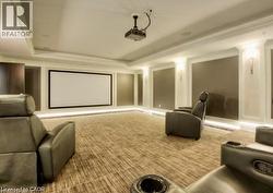 Dedicated media room featuring a large projection screen, ceiling-mounted projector, wall sconces, and recessed cove lighting - 