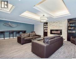 Recessed ceiling lighting with crown molding, stone accent wall with fireplace, built-in shelving, carpet flooring, and a bar area with seating - 